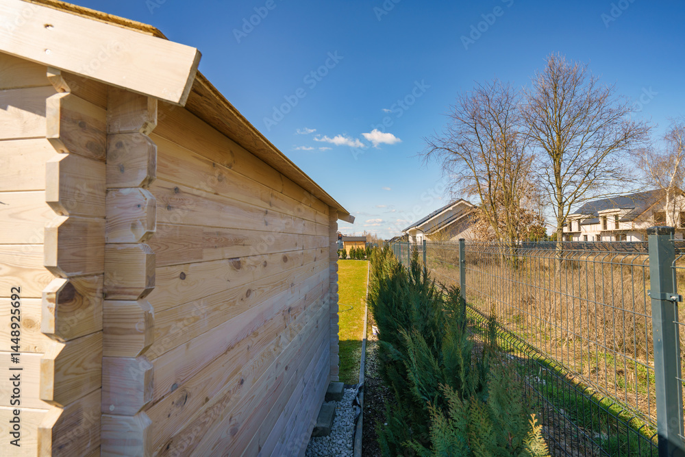 Partly seen wooden shed back wall next to thuja trees and panel fence