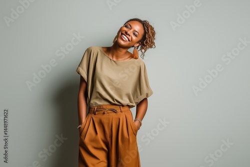Woman smiling with eyes closed in beige top and brown trousers against light blue background