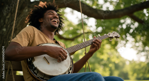Fototapeta Naklejka Na Ścianę i Meble -  Joyful Black man laughing and playing banjo on outdoor swing. Happy African American male musician enjoying folk music in summer garden. Summer fun and creativity concept. USA American culture