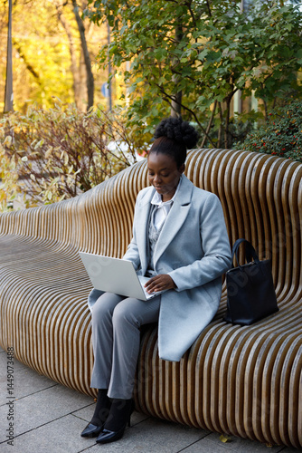 Female copywriter working remotely while sitting on bench in park