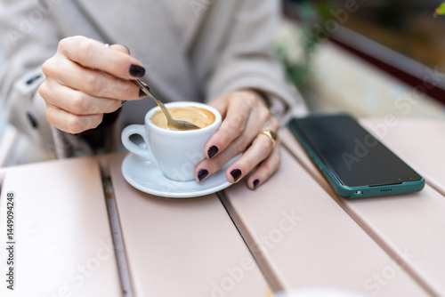 Woman stirring coffee in Bilbao, Spain, with smartphone on table photo