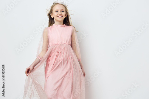 Happy girl in a flowing pink dress posing against a minimalist white background, showcasing joy, innocence, and elegance in a soft, serene atmosphere