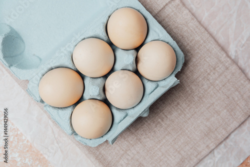 Brown chicken eggs in a blue carton box on light blue background, top view photo