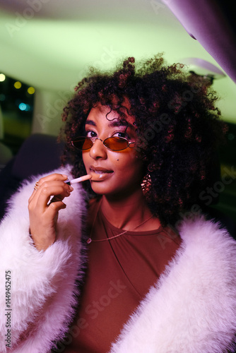 Colorful portrait of cool young woman applying lipstick at night photo
