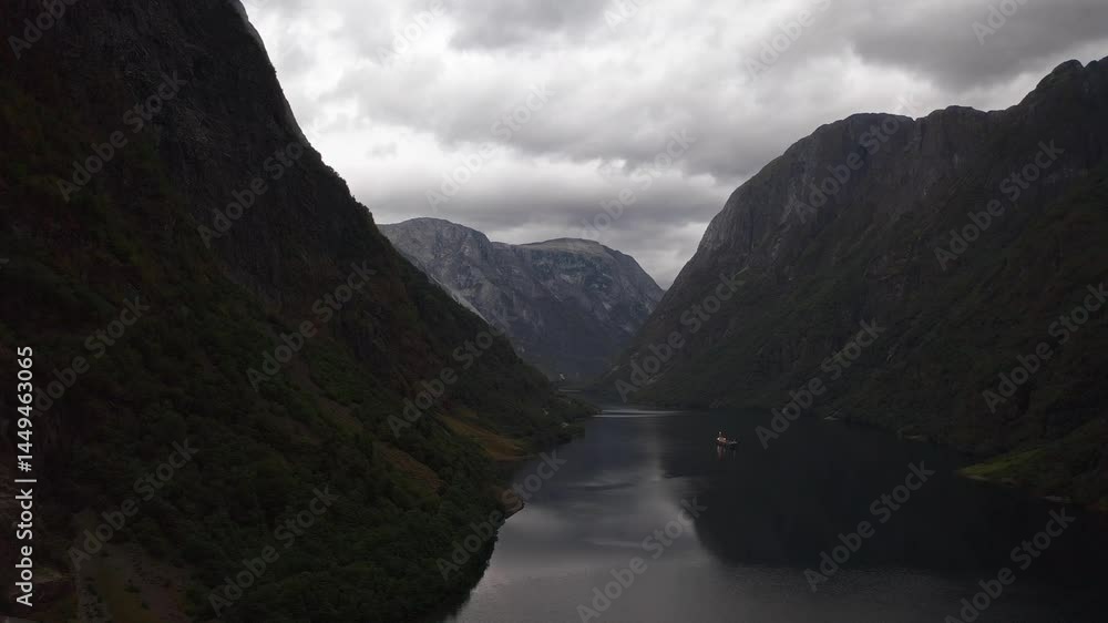 Serene view of a Norwegian fjord, surrounded by towering mountains and cloudy skies Serene view of a Norwegian fjord, surrounded by towering mountains and cloudy skies