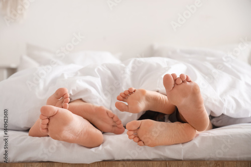 Schilderij op canvas Feet of young man with two women lying under blanket in bedroom, closeup