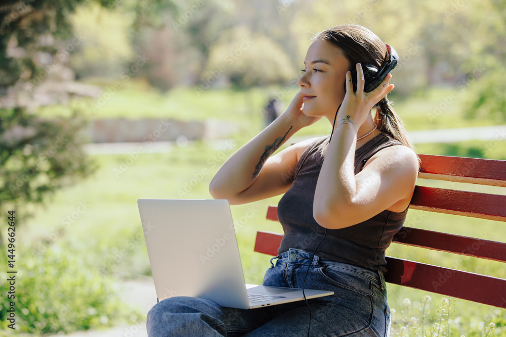 Woman working with laptop wearing headphones sitting on a bench Woman working with laptop wearing headphones sitting on a bench