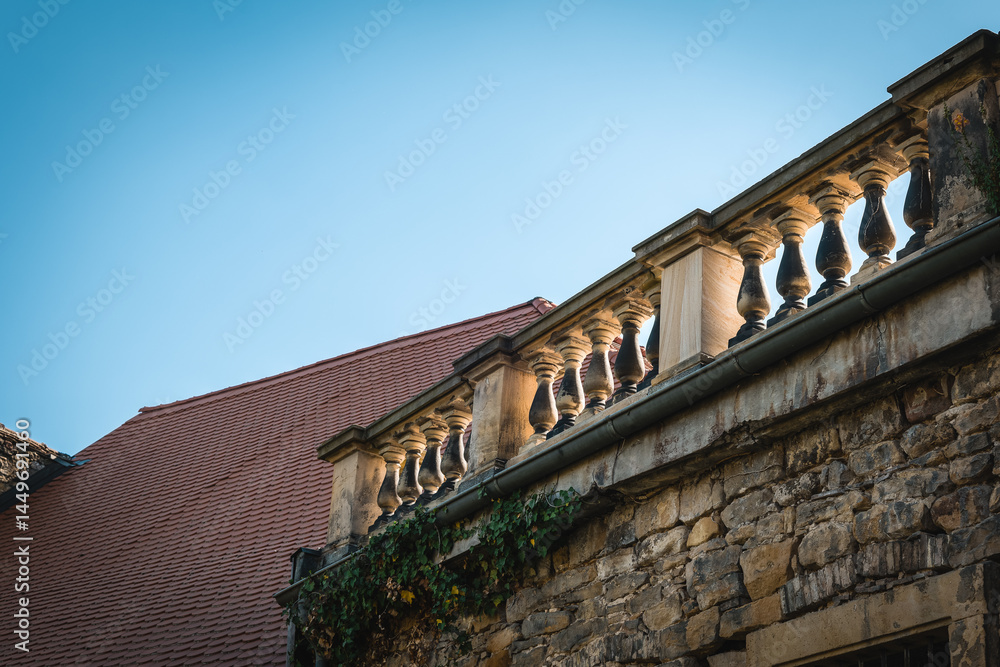 Obraz premium Delicate stone balustrade adorned with intricate designs against the clear blue sky in a historic village setting