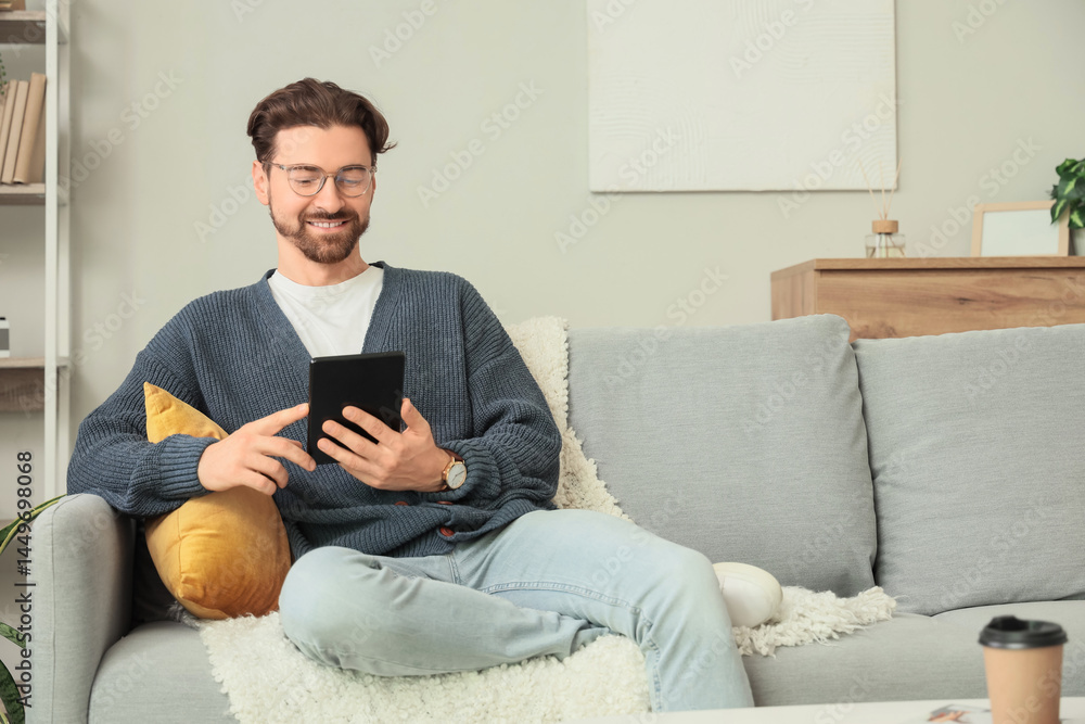 Young man with e-reader sitting on sofa at home Young man with e-reader sitting on sofa at home