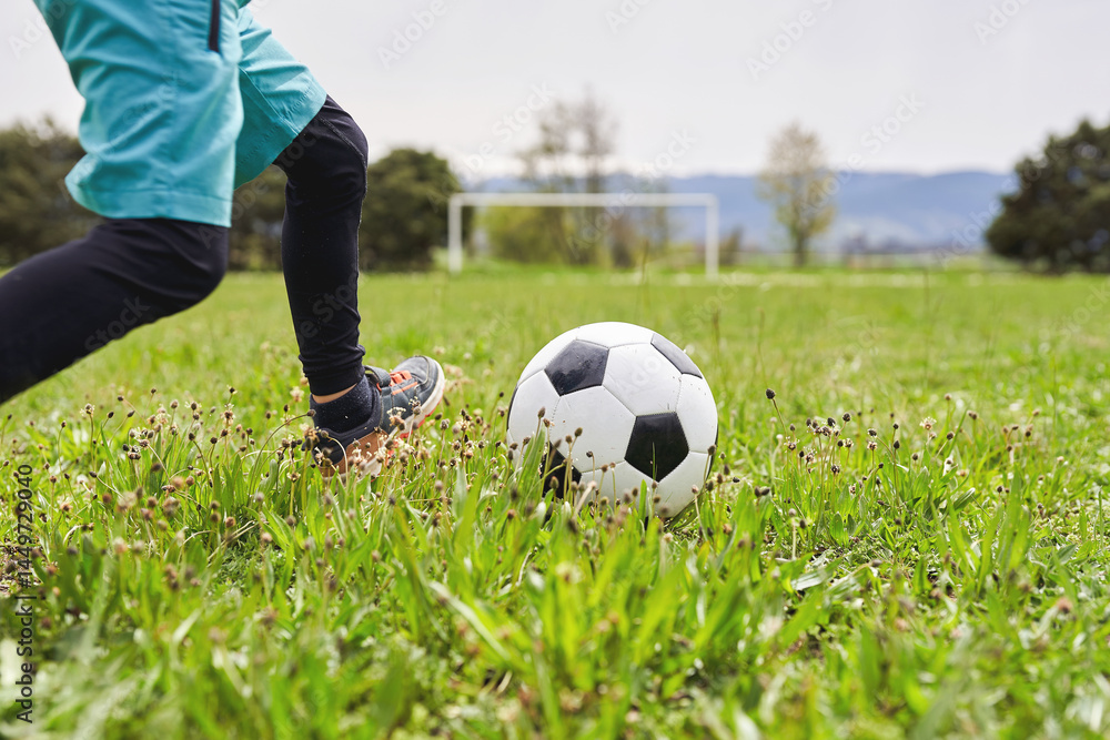 Fototapeta premium Child kicking soccer ball on green field during training session