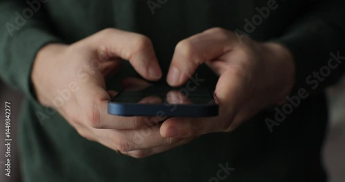 Handsome man using smartphone while spending time at home. Hand typing message for online dating or shopping. Close-up.