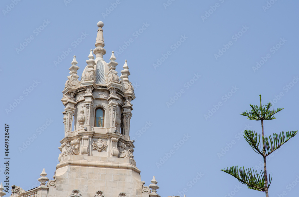 Fototapeta premium March 27 2022 - Spain. Baroque style tower with intricate carvings rises above the building, set against a clear sky and accompanied by a green branch, perfect for architecture or travel themes.