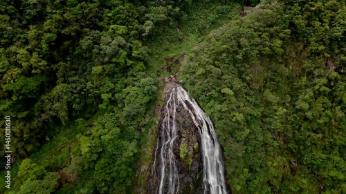 Drone reveals a stunning waterfall cascading through lush tropical mountains. Nature's refreshing spectacle unfolds from above
