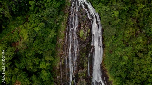 Drone reveals a stunning waterfall cascading through lush tropical mountains. Nature's refreshing spectacle unfolds from above