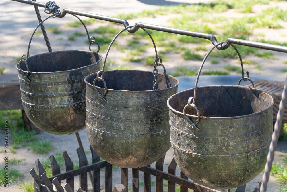 Three metal buckets for cooking hang above a fire pit. Three metal buckets for cooking hang above a fire pit.