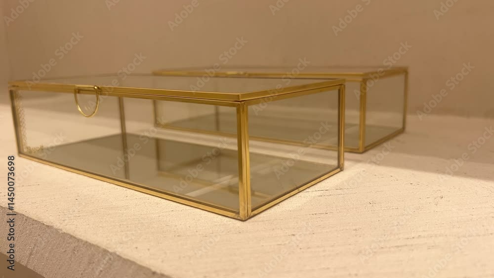 Two elegant glass boxes with gold frames on a light surface, slow motion Two elegant glass boxes with gold frames on a light surface, slow motion