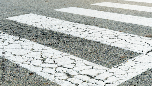 Color of zebra crossing or crosswalk for crossing the road is white. Asphalt road surface with cracks due to age.