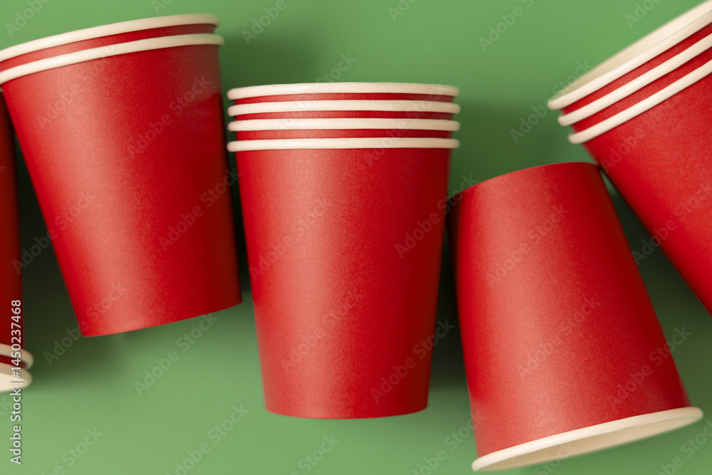 Disposable red paper cups on a green top view, mockup. No plastic and sustainable Christmas