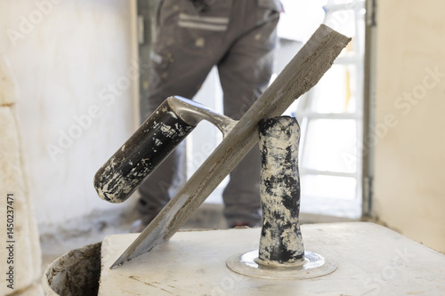 Obraz na płótnie Craftsman in grey clothes working to a doorway during construction, metal trowels in the foreground w salonie