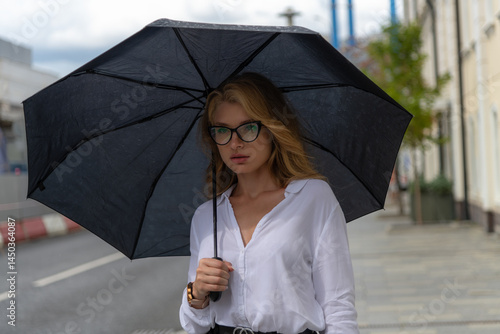 Stylish woman with umbrella walking in the city during rainy day