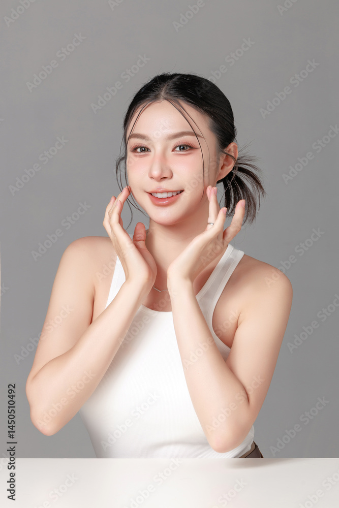Naklejka premium Happy young woman smiling with hands on face against gray background