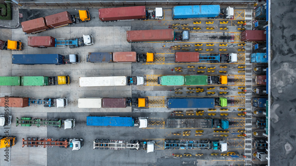 Aerial view semi trailer trucks stand on the parking lot and wait for loading and unloading cargo container at container terminal port, Global business logistic transportation semi trailer trucks.