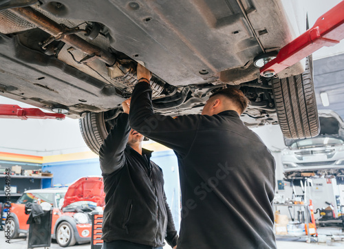 Two mechanics inspecting undercarriage of elevated vehicle in auto repair workshop