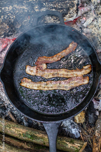 Cooking Bacon Outdoors Over Open Flames with Rustic Cast Iron Skillet