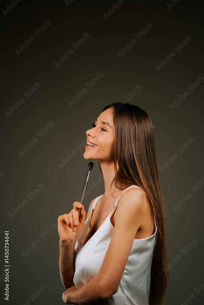 Fototapeta premium Woman smiling while holding a makeup brush with long flowing hair in a dark studio setting