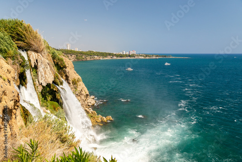 Foto Majestic waterfall cascading into turquoise sea under bright blue sky on vibrant