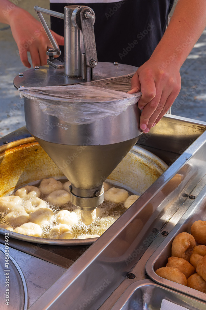 Street vendor frying fresh donuts at outdoor market.
