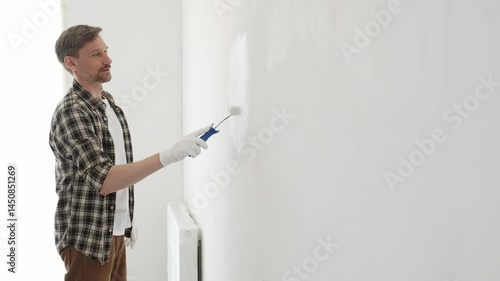 Professional house painter wearing gloves painting a white wall with a paint roller, working on a home renovation project, creating a fresh and clean look