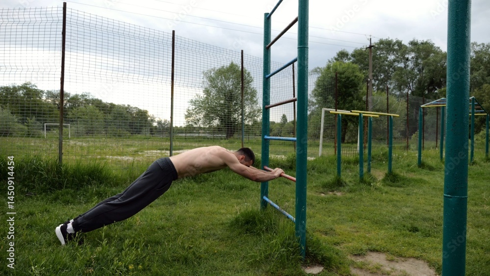 Obraz premium Young muscular athlete doing exercise on triceps at sport equipment outdoor. Male shirtless athlete working out at sport ground. Strong sporty man training at nature. Concept of healthy lifestyle