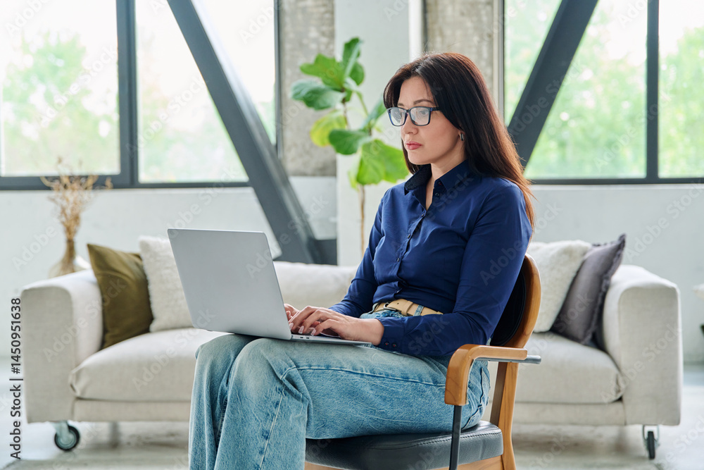 Portrait of serious business woman typing on laptop in office with couch