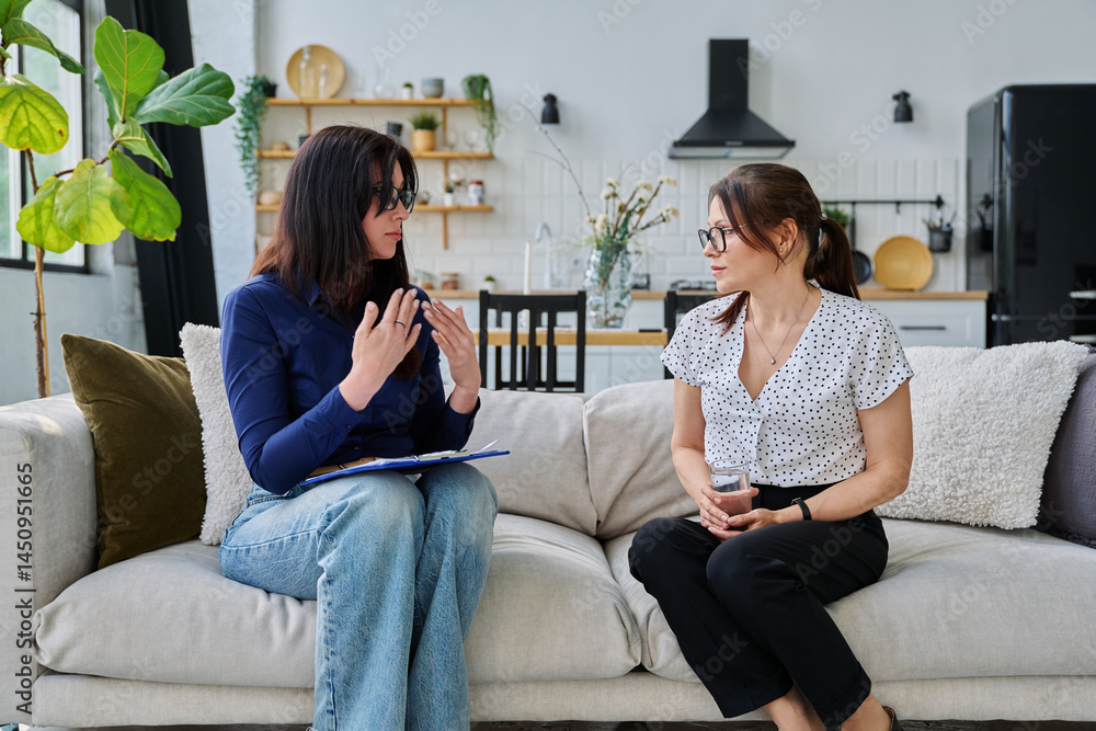 Female social worker interviewing middle aged woman, sitting together in living room