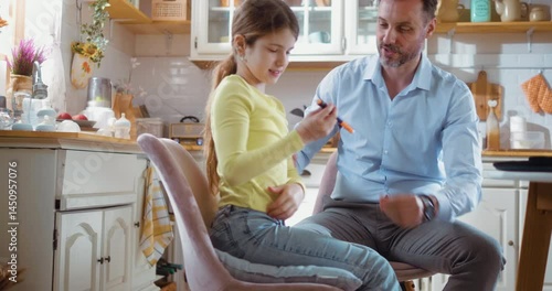 Little girl successfully gives herself an insulin injection with her father's support in the kitchen at home.