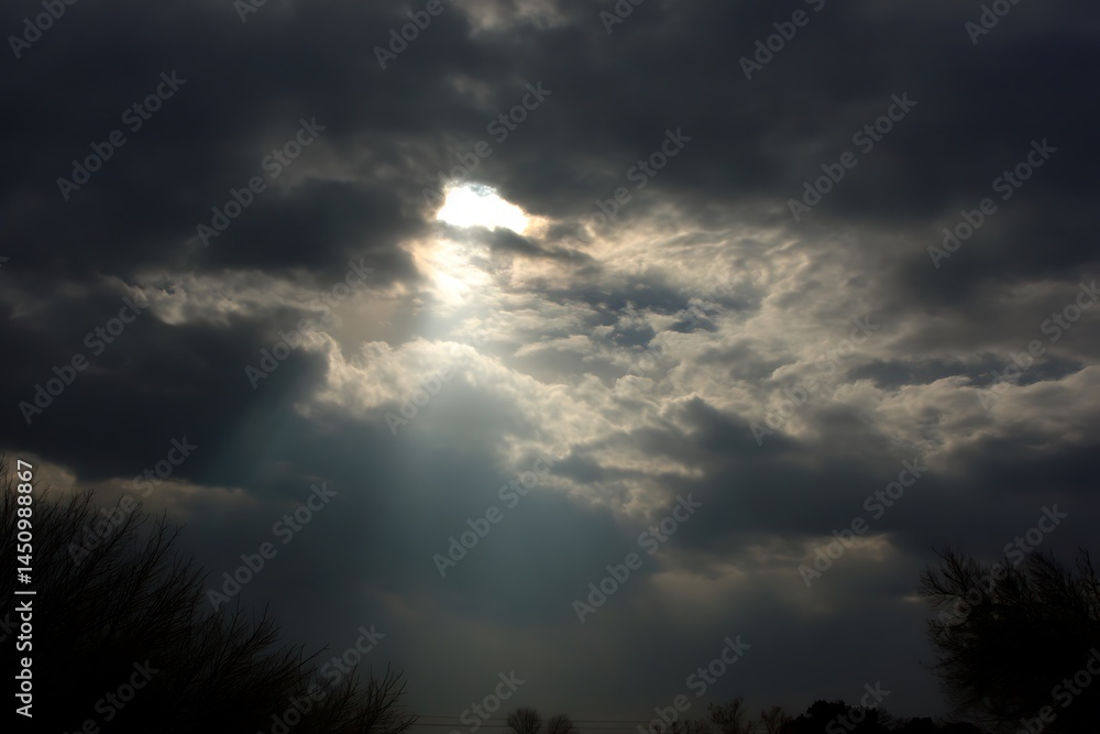 Fototapeta premium Sunlight streaming between grey clouds view 
