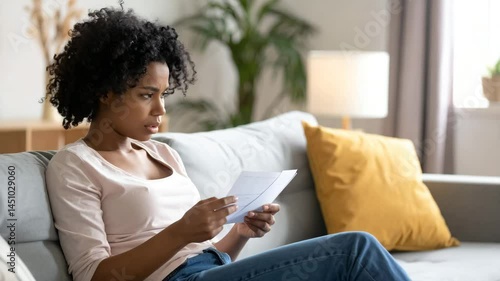 Concerned Woman Reading Letter Alone on Couch in Natural Lighting