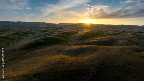 Aerial view of gently rolling grasslands at sunset with clouds in sky