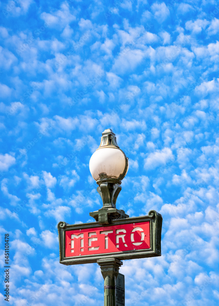 Parisian metro sign in red with a lamppost with blue soft cloudy sky