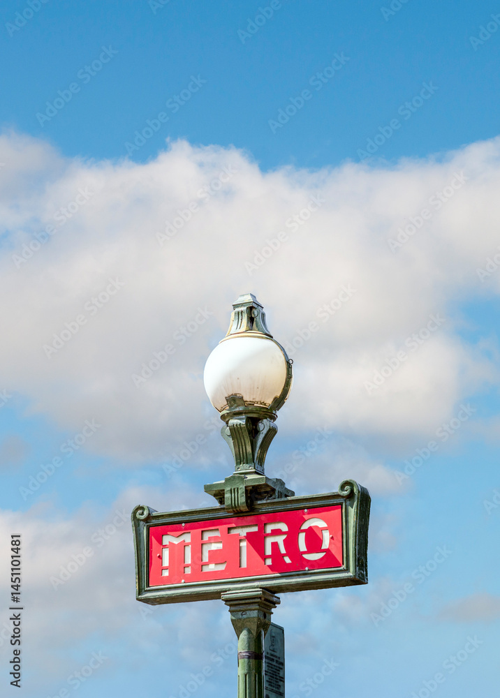 Parisian metro sign with a lamppost with puffy soft blue sky
