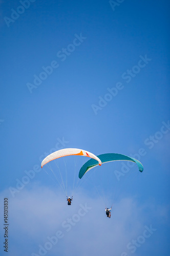 Obraz na płótnie A pair of paragliding athletes are floating in the air showing their skills in controlling their paraglider against a backdrop of bright blue sky. w salonie