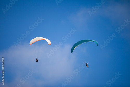 Obraz na płótnie A pair of paragliding athletes are floating in the air showing their skills in controlling their paraglider against a backdrop of bright blue sky. w salonie