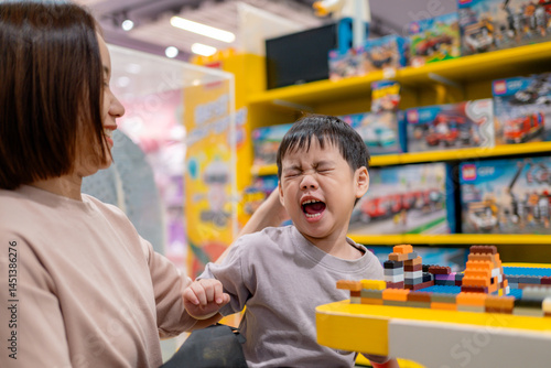 Fototapeta Stubborn child refusing to leave toy store while building with colorful bricks,