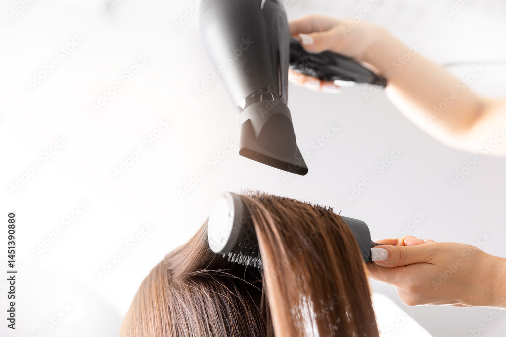 Naklejka premium Professional hair styling with blow dryer and brush at salon