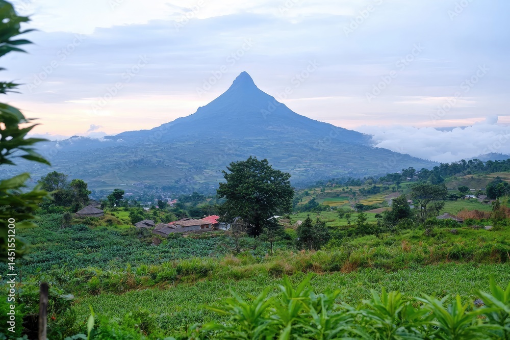 Fototapeta premium Serene landscape featuring a majestic, pointed mountain rising above lush green fields and a small village