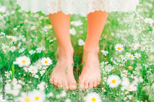 Green grass female legs. Female legs  and fresh flower.A photo of a person's feet resting on the grass. A person walking barefoot on grass, highlighting the sensory connection with earth.