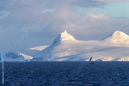 Obraz na płótnie An Antarctic landscape, taken during the golden hour, just after sunrise, in the Gerlache Strait. A little sailboat in the foreground explores the Antarctic waters. w salonie