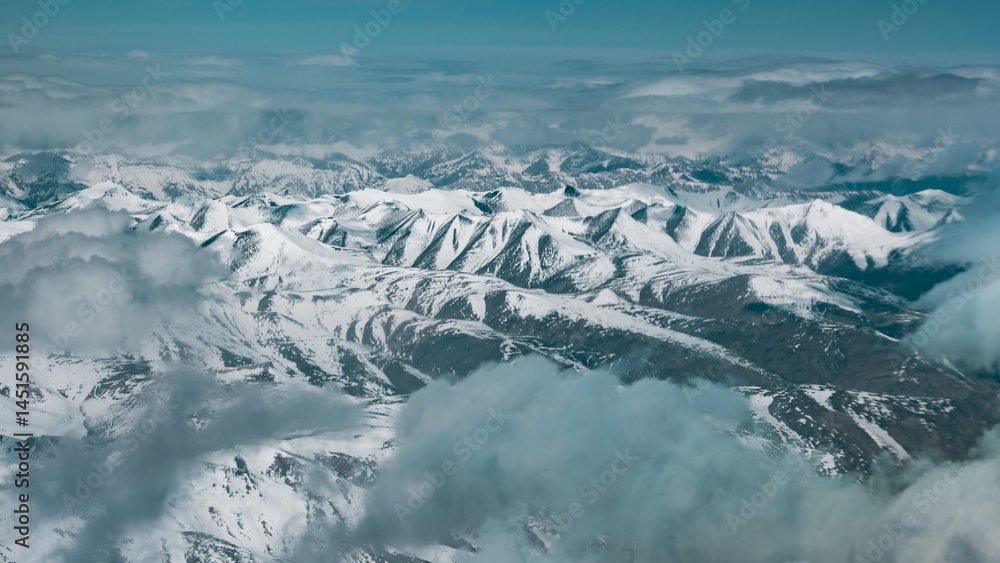 Fototapeta premium breathtaking aerial view of the snow covered peaks of the Himalayas, showcasing dramatic cliffs, deep valleys and serene glaciers under blanket of clouds in the world highest mountain range