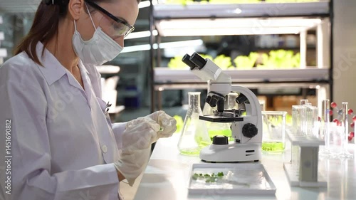 Female researcher injecting liquid to test tube while observing microgreens under lab microscope
